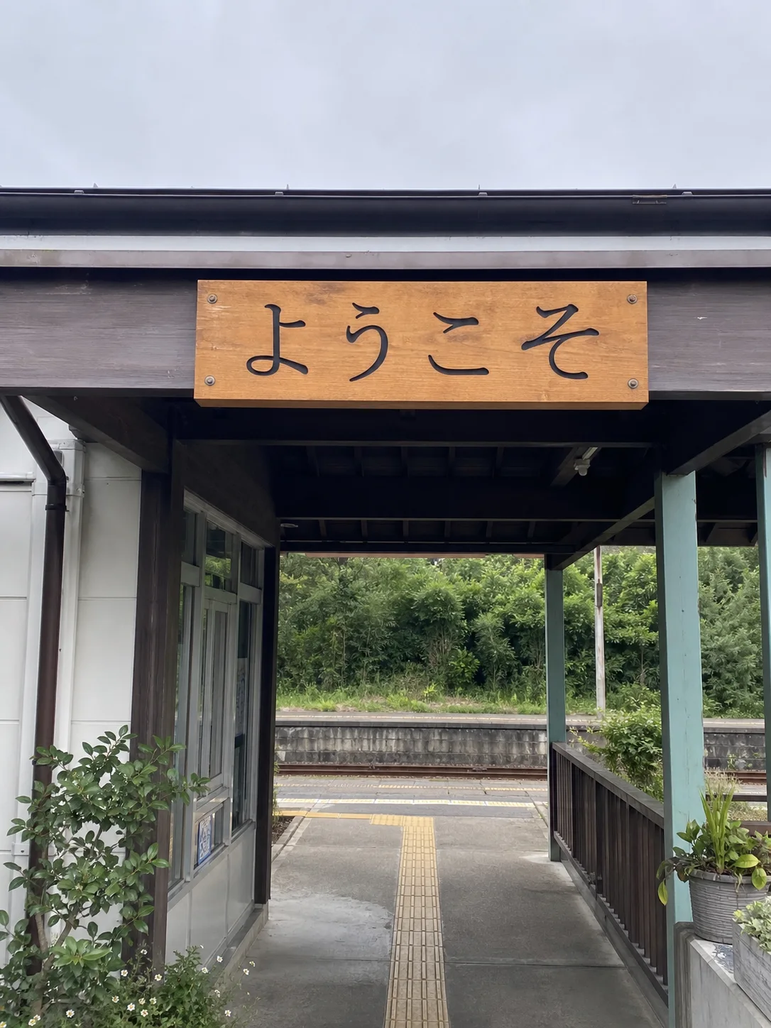 A Japanese station entrance with a handwritten ようこそ welcome sign
